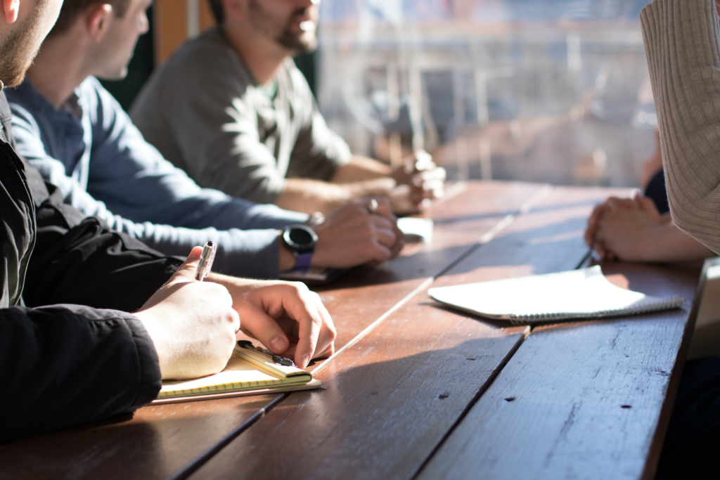 people sitting on chair in front of table while holding pens during daytime
